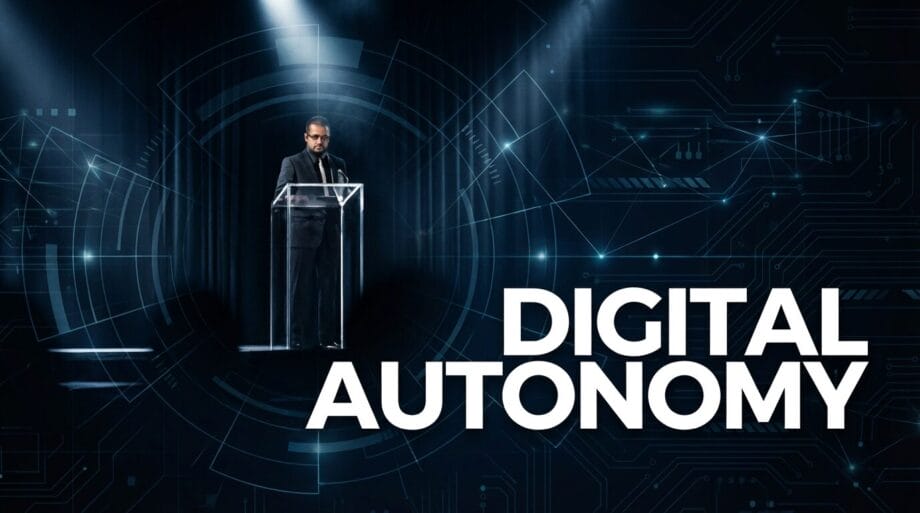 A man stands at a clear podium on stage with the words DIGITAL AUTONOMY displayed beside him over a digital circuit background.