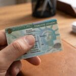 A person holds a U.S. Permanent Resident Card at a desk with office items in the background.