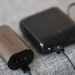 Two portable power banks are connected by a charging cable, resting on a grey fabric surface.
