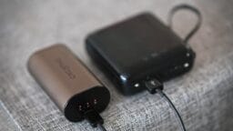 Two portable power banks are connected by a charging cable, resting on a grey fabric surface.
