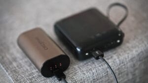 Two portable power banks are connected by a charging cable, resting on a grey fabric surface.