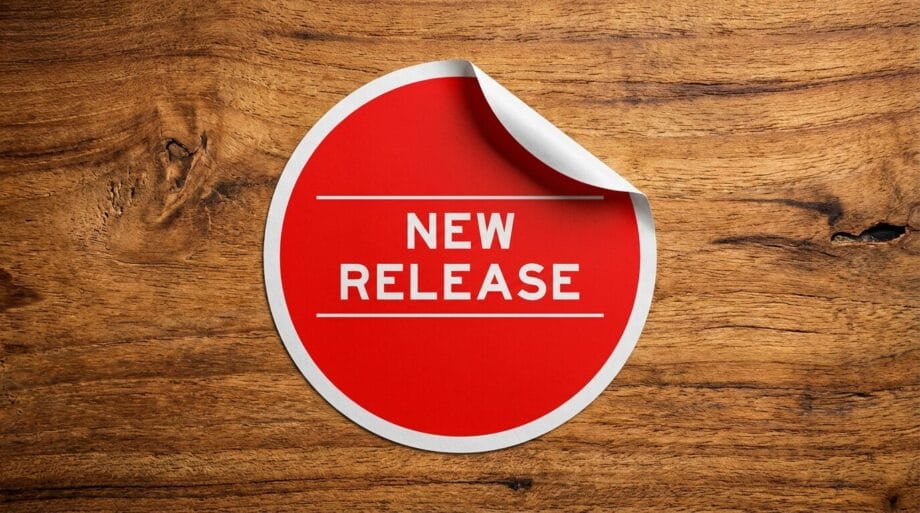 A red sticker with the words NEW RELEASE on a wooden surface; the top right edge of the sticker is slightly peeled up.