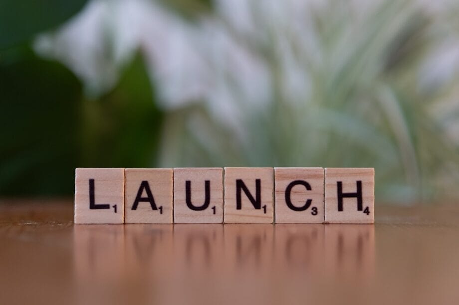 Wooden letter tiles on a wooden surface spell out the word LAUNCH with a blurred green and white background.