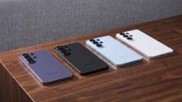 Four Samsung smartphones in different colors are displayed face down on a wooden surface against a gray background.