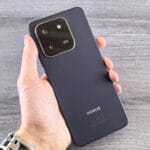 Hand holding a dark blue smartphone with camera module.