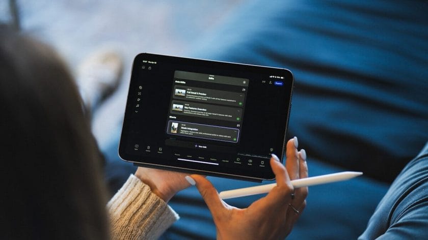 Person holding a stylus and using a tablet with a dark-themed app interface displaying a playlist or series of media options.