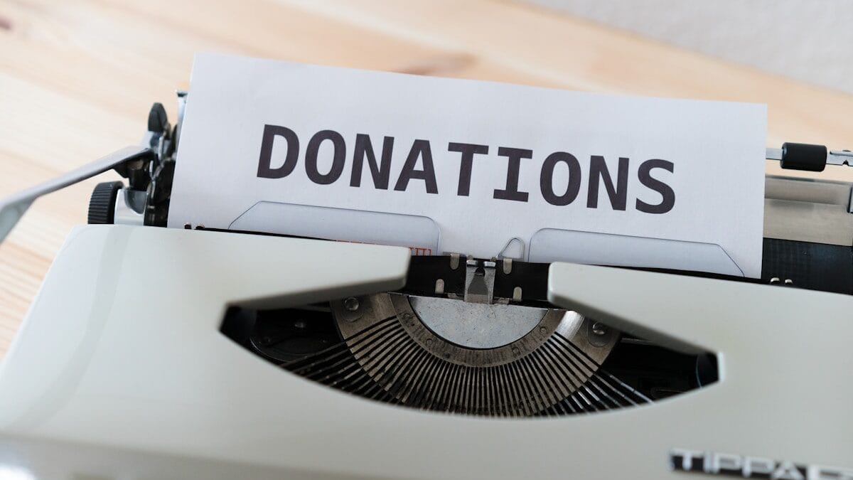 A sheet of paper with the word DONATIONS is inserted into a white typewriter on a wooden surface.