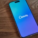 A smartphone displaying the Canva app logo on its screen rests on a wooden surface.