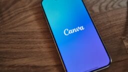 A smartphone displaying the Canva app logo on its screen rests on a wooden surface.