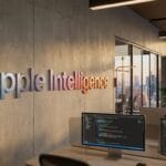 Modern office space with Apple Intelligence sign on the wall and computer workstations in the foreground.