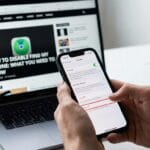 Person holding an iPhone with settings open, sitting in front of a laptop displaying a tech article about disabling Find My iPhone.