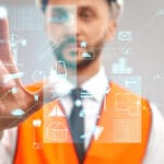 A person in a hard hat and orange vest interacts with virtual construction-related icons on a transparent digital interface with computer vision technology.