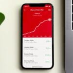 A smartphone displaying a Youtube subscriber growth chart and numbers, next to a laptop and a green plant on a white surface.