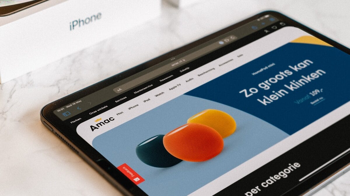 A tablet displays a website in Dutch with colorful speaker images, lying on a marble surface near an iPhone box.