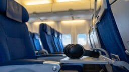 A pair of black headphones rests on the open tray table of an empty airplane seat in the cabin.