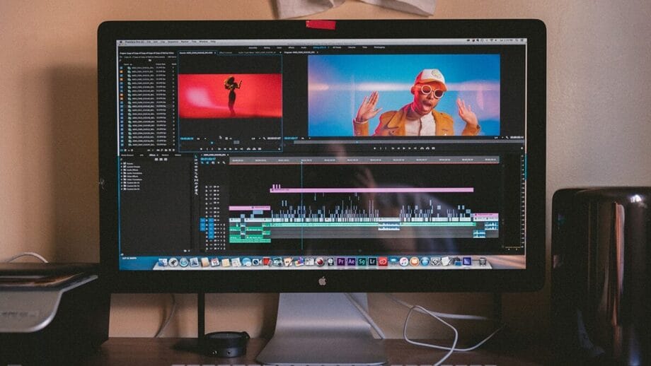 A desktop computer displaying video editing software with a music video in progress, featuring a person wearing red sunglasses and a white cap.