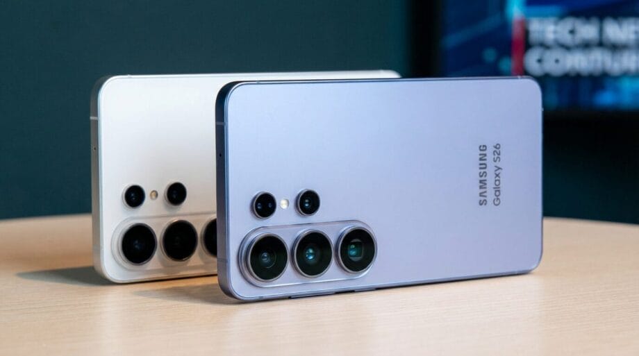 Two Samsung Galaxy S24 smartphones with triple rear cameras are displayed on a wooden surface, one silver and one cream colored.