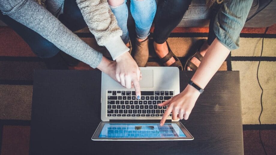 Three people sitting on a couch point at a laptop screen on a table, collaborating on something together.