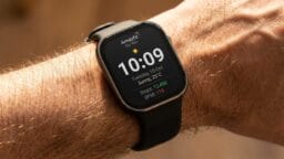 A smartwatch on a persons wrist displays the time, date, weather, step count, and heart rate on its home screen.