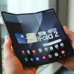 Person holding an open foldable smartphone displaying its main home screen with various app icons and a large “Fold 2” on the display.