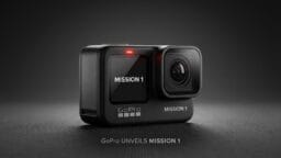 A black GoPro camera labeled MISSION 1, with a lit indicator and screen displaying MISSION 1, on a dark textured surface.