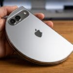 A hand holding a silver Apple smartphone with a distorted, semi-circular shape on a wooden surface.