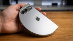 A hand holding a silver Apple smartphone with a distorted, semi-circular shape on a wooden surface.