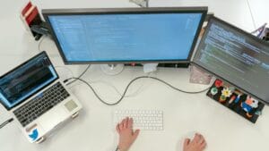 Person working at a desk with a laptop and two monitors displaying code, viewed from above.