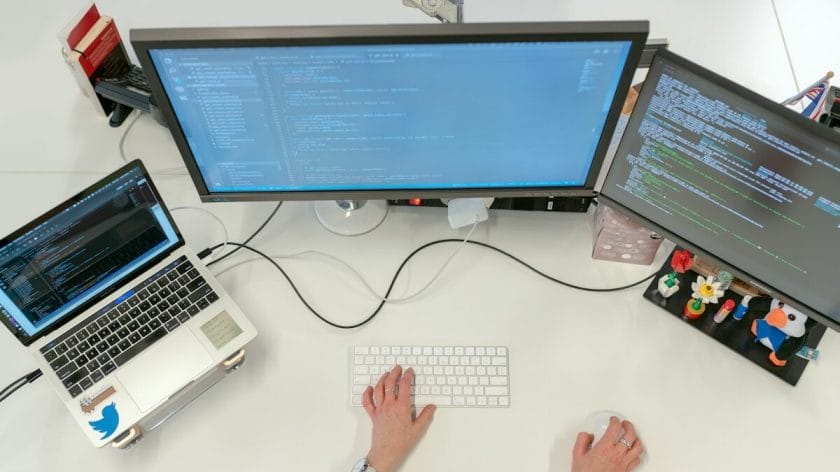 Person working at a desk with a laptop and two monitors displaying code, viewed from above.
