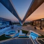 Futuristic Ola facility with electric scooters on the left, taxi service on the right, and illuminated paths converging at sunset.