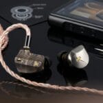 A pair of high-end in-ear monitors with braided cable lies next to a digital audio player on a glossy black surface.