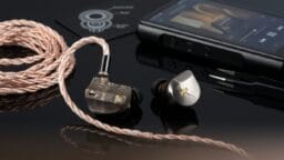 A pair of high-end in-ear monitors with braided cable lies next to a digital audio player on a glossy black surface.