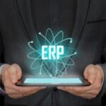 A person in a suit holds a tablet with a digital hologram displaying the letters ERP above it.