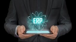A person in a suit holds a tablet with a digital hologram displaying the letters ERP above it.