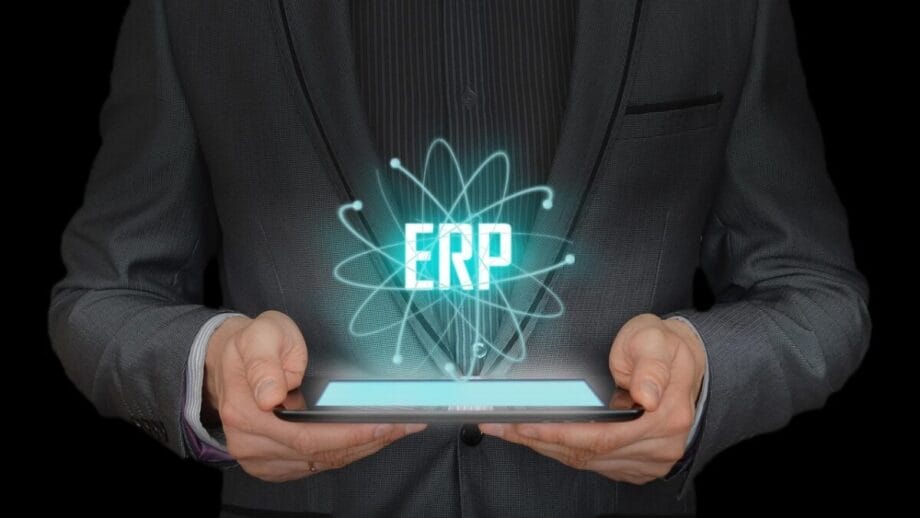 A person in a suit holds a tablet with a digital hologram displaying the letters ERP above it.