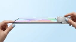 A smartphone is held sideways as a ruler measures its thinness against a light blue background.