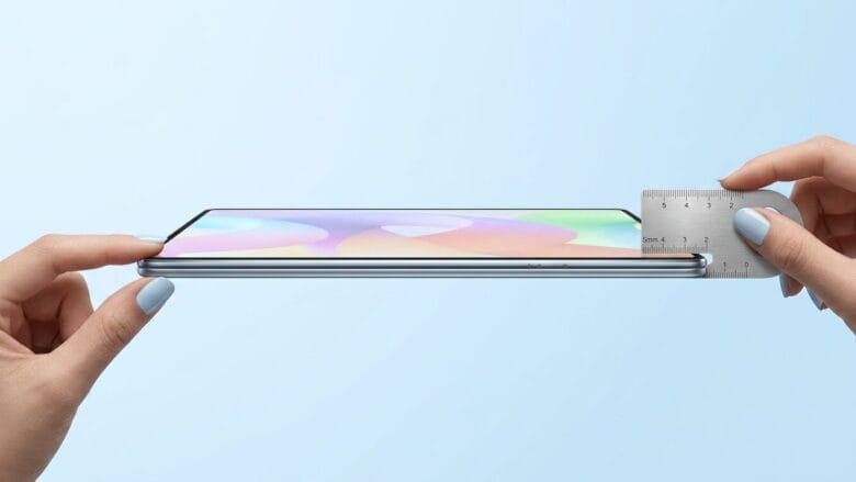 A smartphone is held sideways as a ruler measures its thinness against a light blue background.