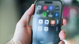 A hand holds a smartphone displaying an AI folder with five artificial intelligence app icons on the screen.